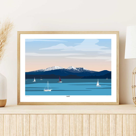 A framed travel poster depicting a scenic view of mountains and a lake with sailboats, titled 'Tranquil Peaks', representing New Zealand.