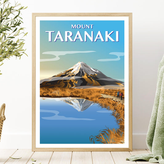 A framed vintage style travel poster depicting Mount Taranaki, showing the mountain in autumn with a clear sky and reflection in water. The frame is gold-colored.