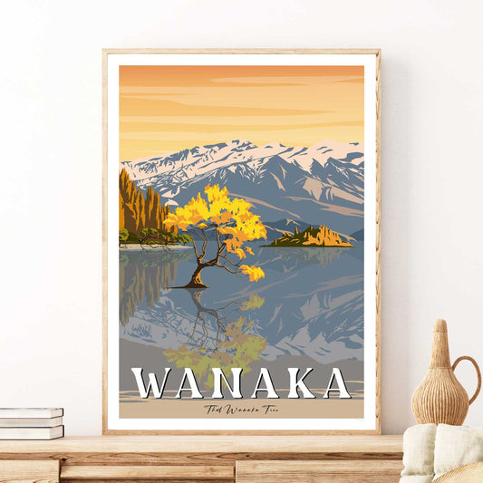 A framed travel poster depicting 'That Wanaka Tree' with a scenic view of the tree, lake, and mountains in the background, indicating Autumn.