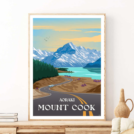 Travel poster depicting Aoraki Mount Cook with a winding road leading up to it, surrounded by mountains, a lake, and a clear sky. The name 'Aoraki Mount Cook' is prominently displayed at the bottom.