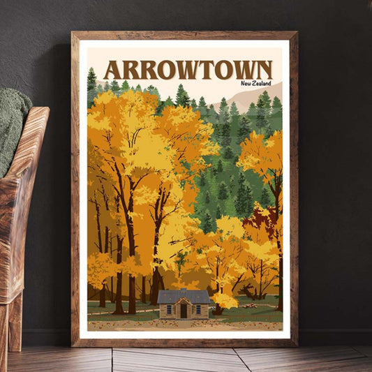 A framed travel poster depicting the Arrowtown old police hut surrounded by trees in autumn colors, displayed on a wall.