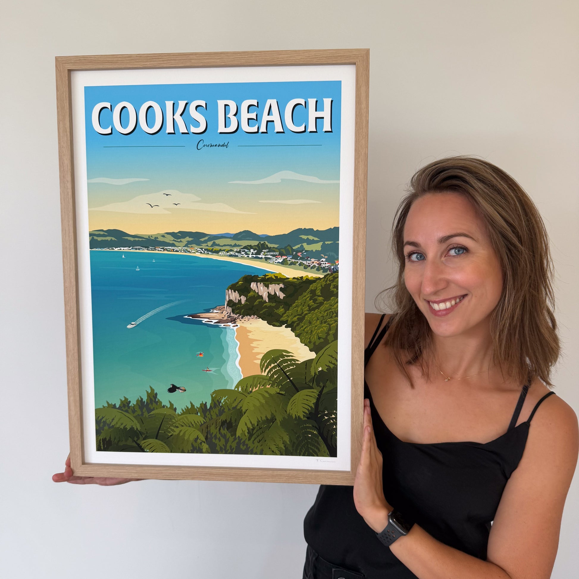 Woman holding a framed artwork of Cooks Beach with a scenic view.