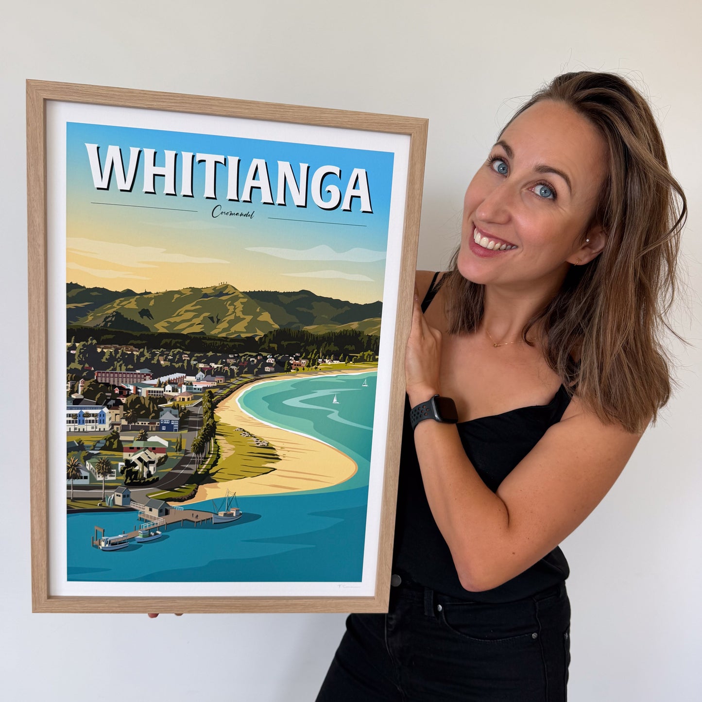 Woman holding a framed poster of Whitiana with a scenic view.
